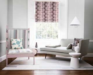 Chic living room with pattern rug and chair pillows, plus gray chaise longue, and window with blinds pulled half way down