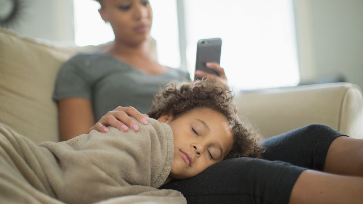 Mother and daughter snuggling on sofa, child is sleeping on mothers lap