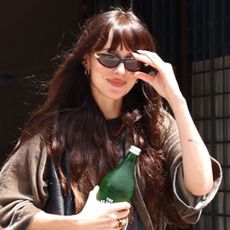 Dakota Johnson wears baggy jeans, white and green sneakers, and sunglasses