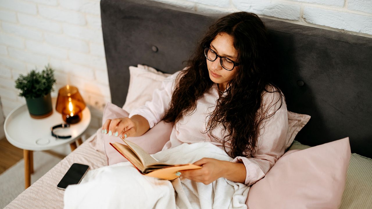 Woman sitting up in bed turning page of a book