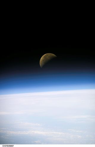 A quarter moon rises above Earth's horizon and above the airglow of our atmosphere. The image was made with a digital still camera on the final mission of the Space Shuttle Columbia. Columbia's crew was killed on Feb. 1, 2003, when the shuttle broke up on re-entry into Earth's atmosphere.