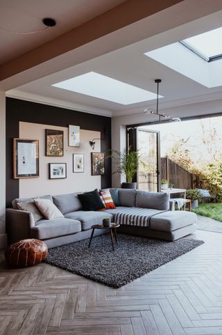 A low slubby sofa in living room with Herringbone detail wooden flooring and framed wall art