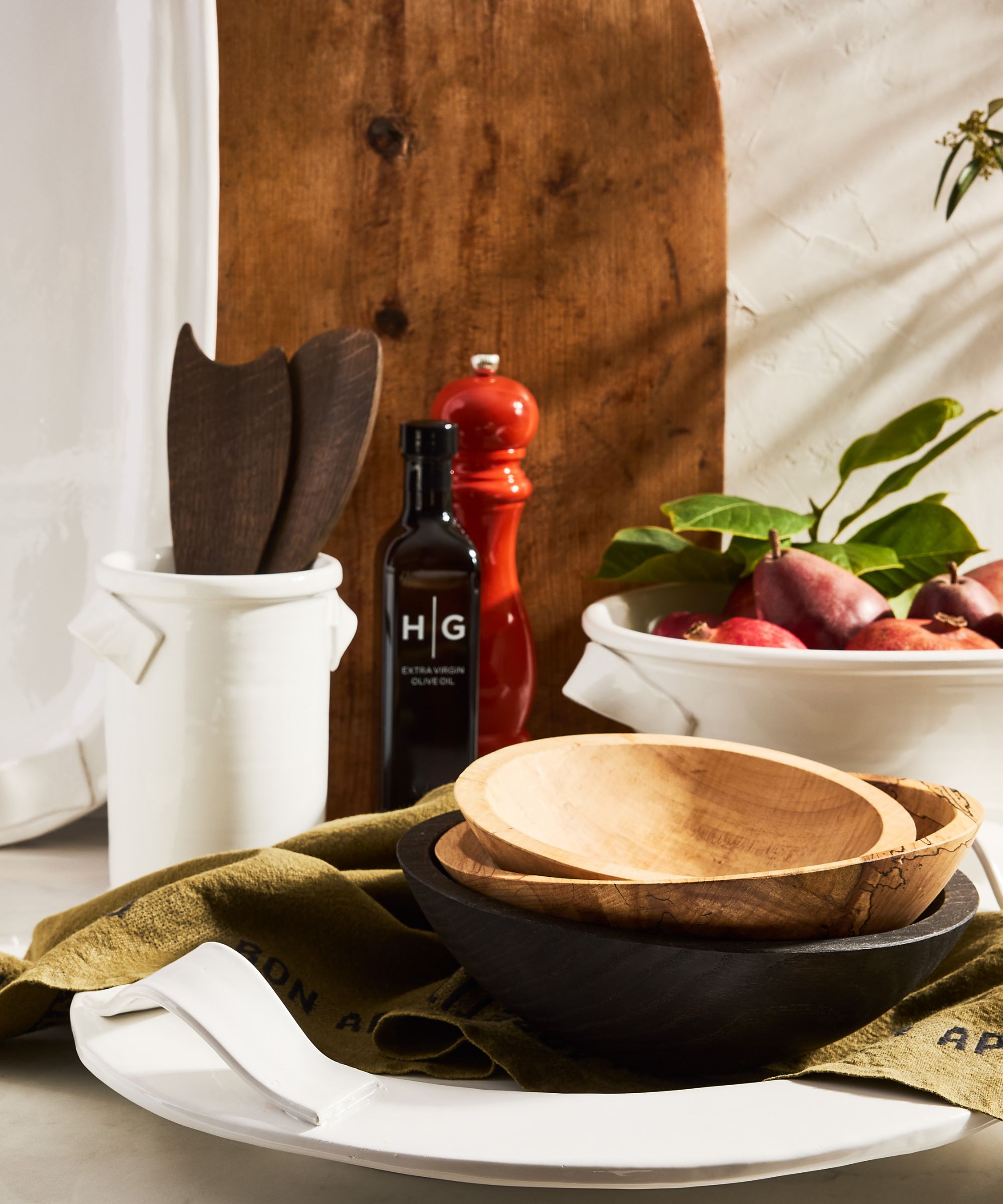 Table with white stone plates, olive green linen napkins, wooden serving bowls and platters and red salt and pepper mills