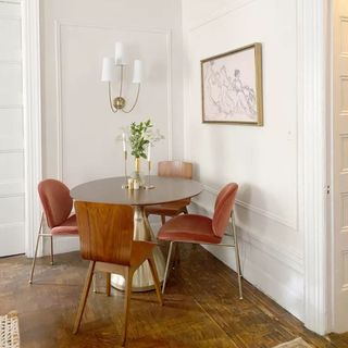 Round wooden dining table in corner with leather black chairs, white flowers in vase and wall sconce