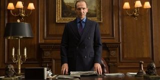 Spectre M standing at his desk, in a double breasted suit