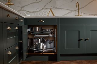 dark green kitchen with open corner cabinet, brass taps, and marble splash back