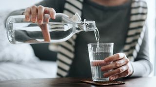 person pouring water from a bottle into a glass to stay hydrated to show how to keep cool in summer