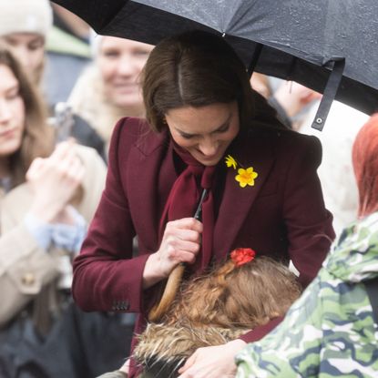 Princess Kate hugging a little girl while holding an umbrella