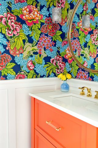 bright powder room with floral wallpaper and orange vanity unit by Kim Armstrong Design