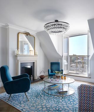 Monochromatic apartment living room ideas illustrated in blue and white, with white walls and blue armchairs and rug, alongside a glass chandelier and glass doors leading onto a small balcony.