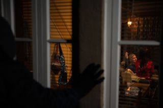 Someone in a hood watching Leyla Harding and Caleb flirting through a window. 