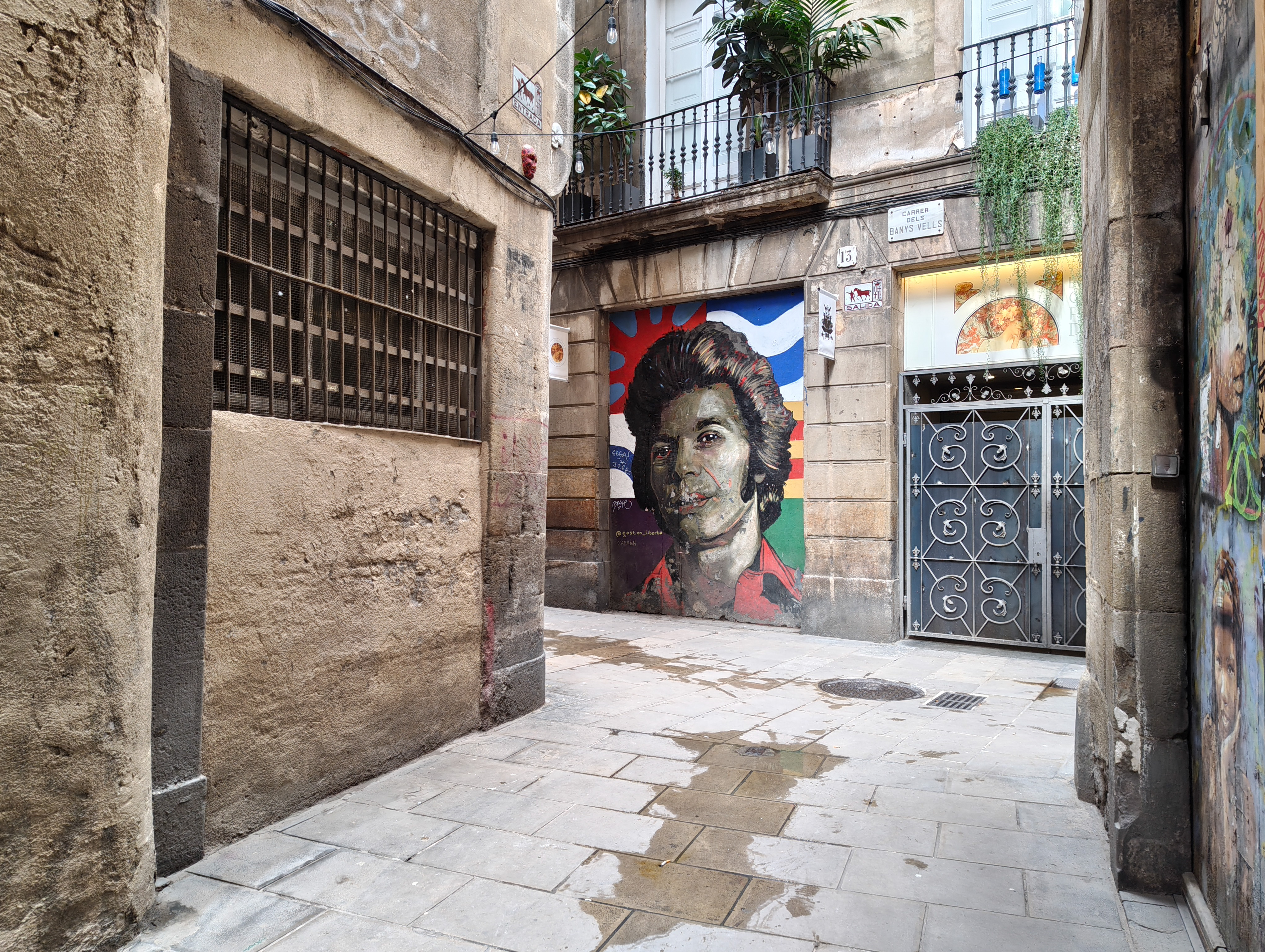 Narrow alley with historic buildings and a large mural portrait painted on a wall in Barcelona, photographed with the Nothing Phone (4a).