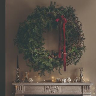 A fireplace decorated with fairy lights and an oversized wreath with a red bow hanging on the wall above it