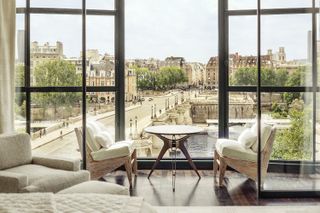 A white hotel bedroom with windows open to a view of Paris