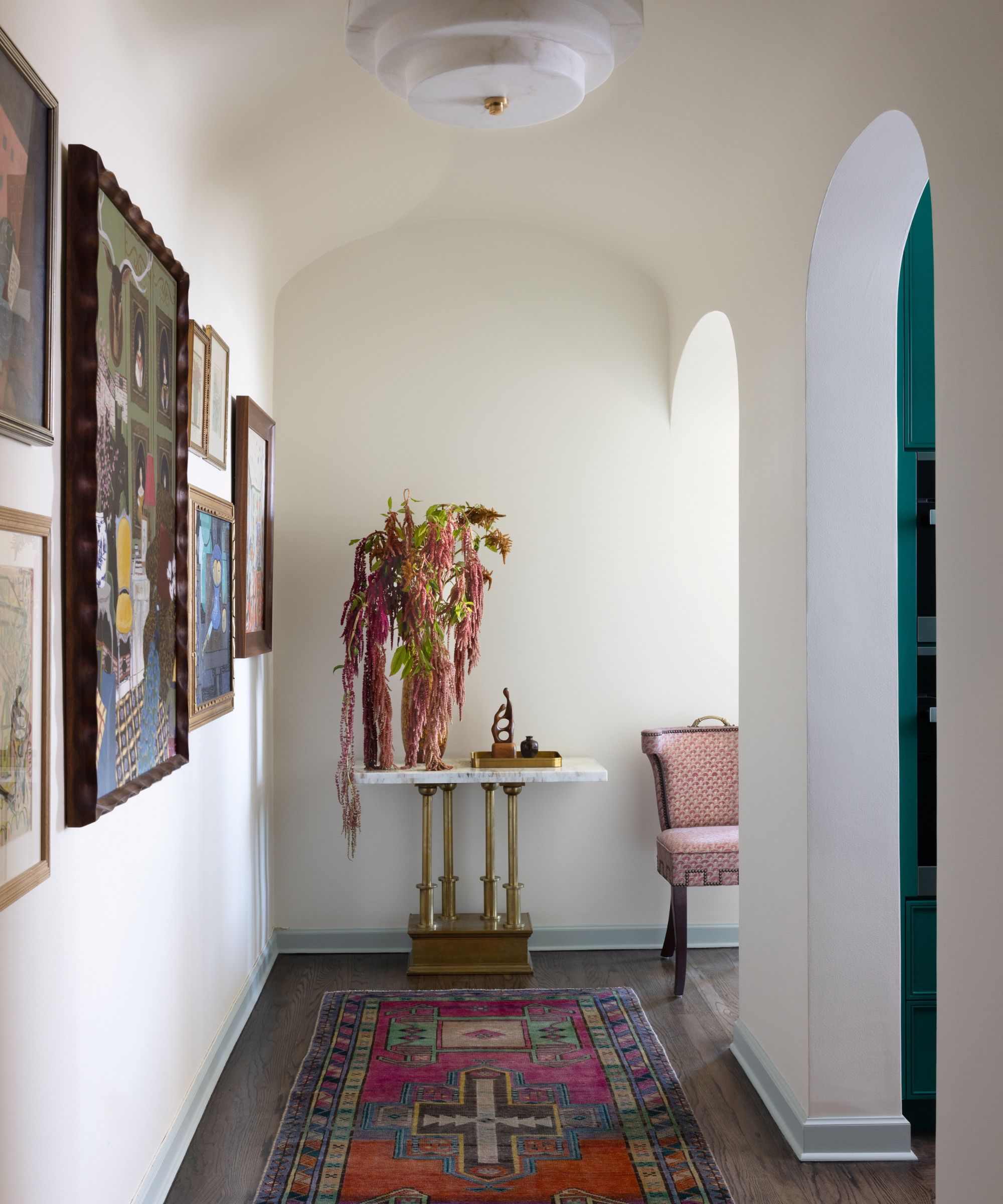Small entryway with arched doors and a gallery wall on one side, a Persian rug-style runner and gold and marble console table at the end