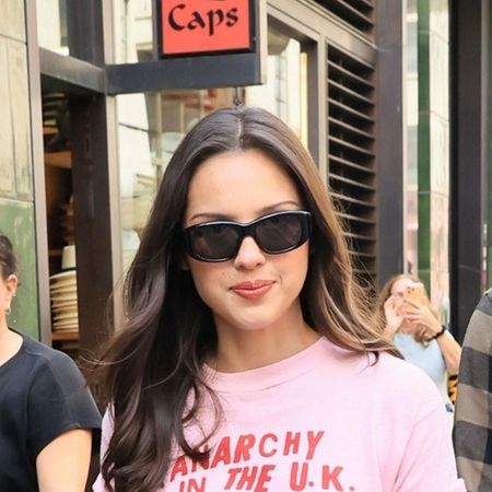Olivia Rodrigo wearing a pink graphic t-shirt, leather mini skirt, black knee-high boots, and black sunglasses
