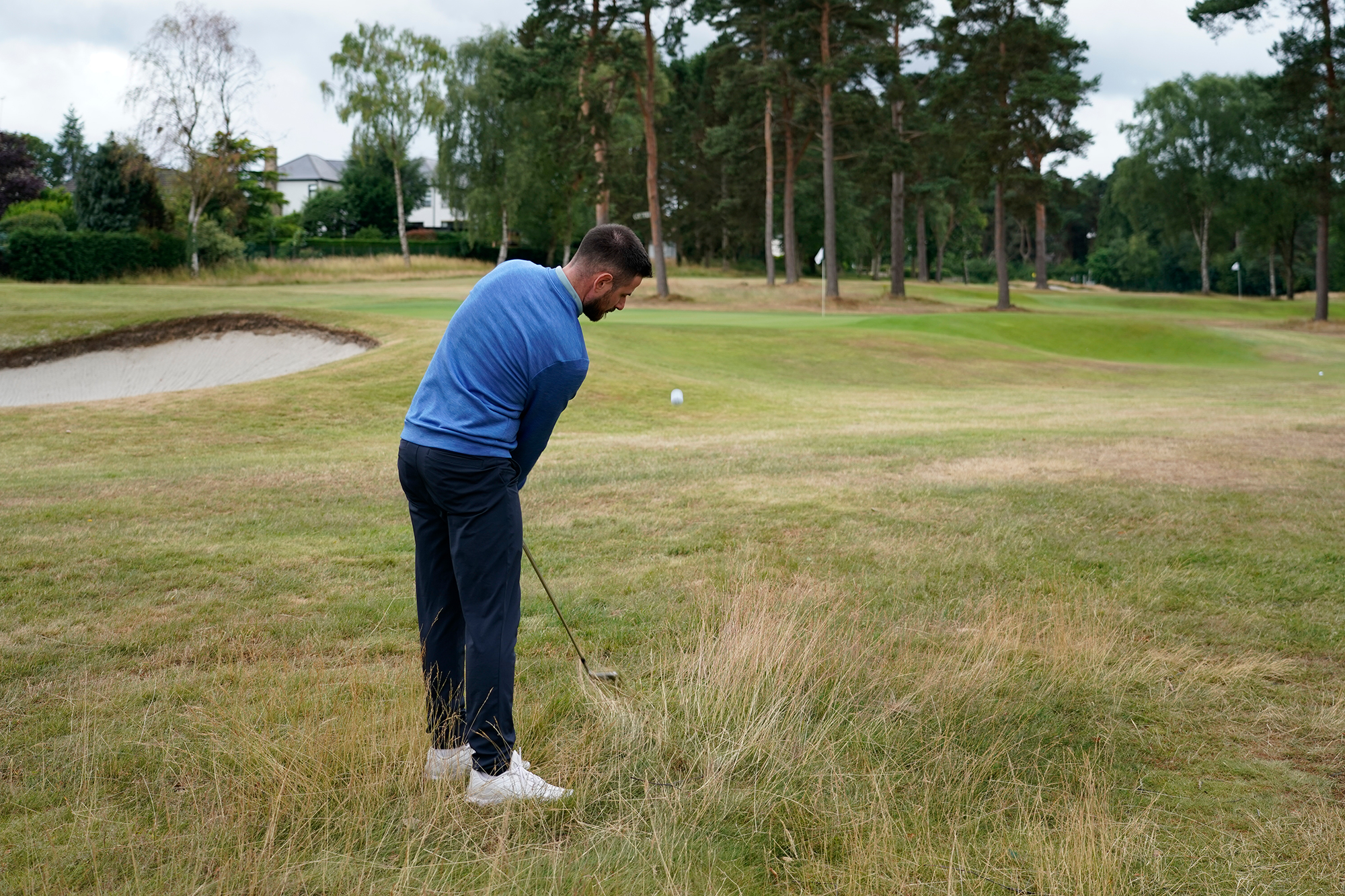 Baz Plummer hitting a high-flighted chip shot out of long grass to the right hand side of the first green at Sand Moor Golf Club
