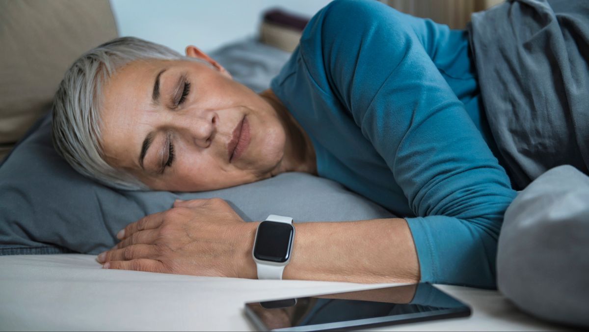 Woman sleeping on her side with a smart watch on her wrist and her phone on the bedside table