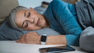 Woman sleeping on her side with a smart watch on her wrist and her phone on the bedside table