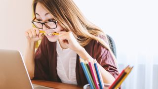 Woman biting pencil as she looks at student discounts on laptop