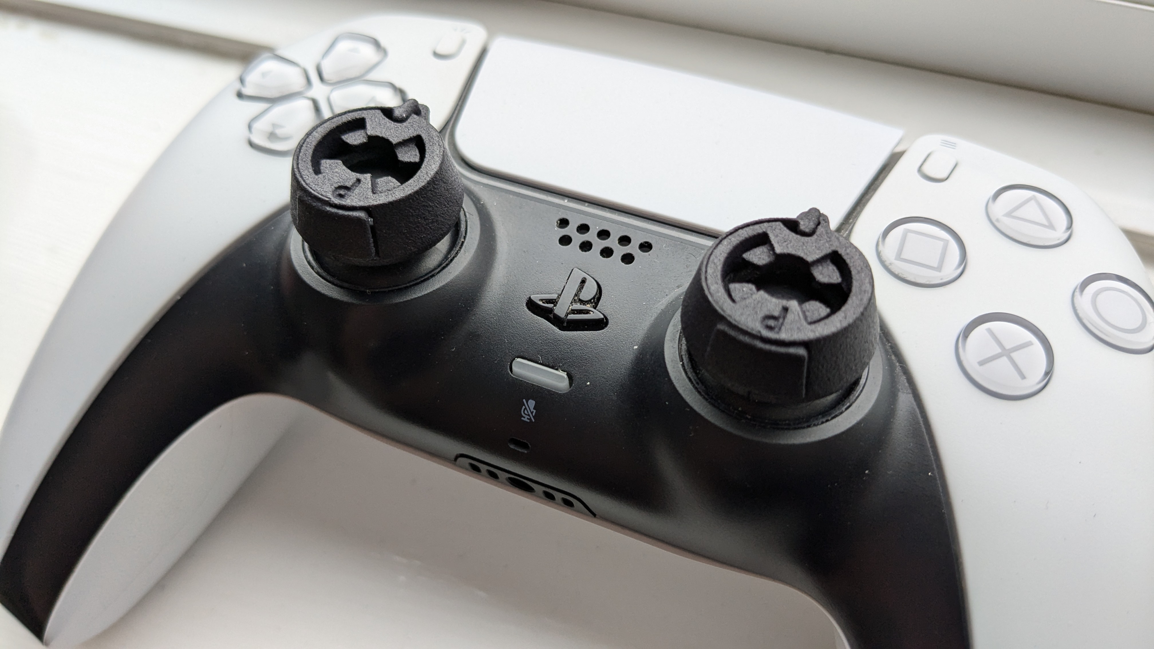 A DualSense Wireless Controller with two Thumb Soldier attachments on each stick.