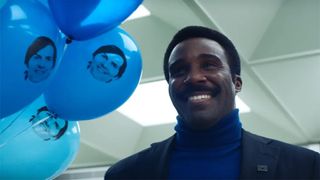 Tramell Tillman smiles next to balloons with Mark Scout's face 