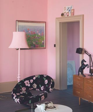 A pink living room with a wall art print, lamp, floral chair, and coffee table