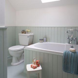 white bathroom with mint green painted panelling on half the wall and up the bath surround