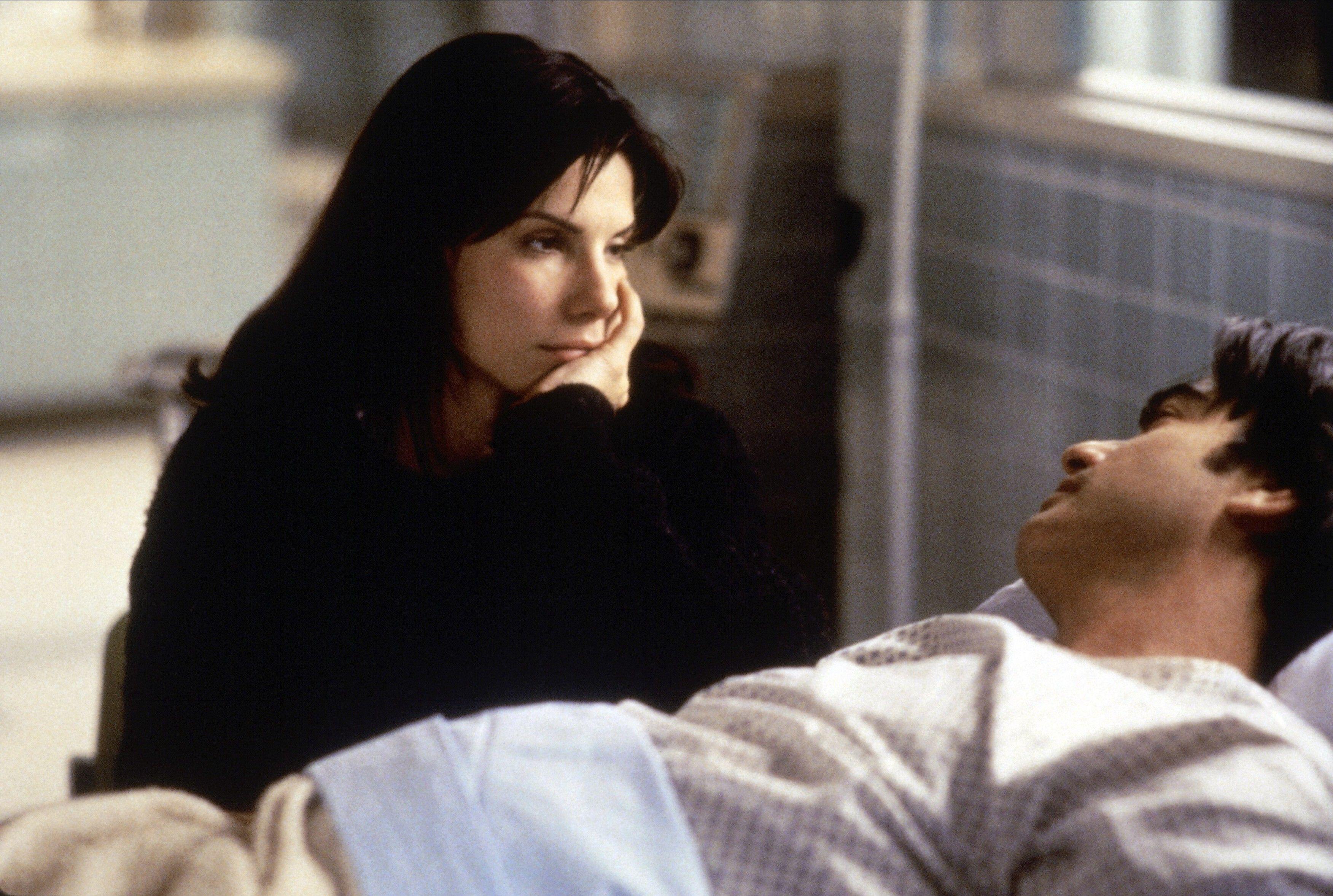 Sandra Bullock looks at a sleeping man in a hospital bed in 'While You Were Sleeping'