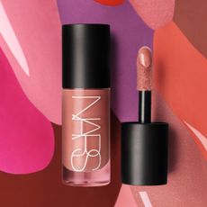 A glass, tube-shaped bottle with the word NARS written in white letters. It also has a black top, and there is a black top with a doe foot applicator next to it.