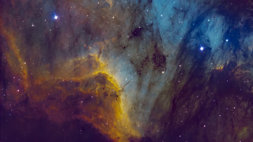 White-blue stars are pictured shining against a nebula backdrop, which is a mixture of colorful gas overlaid by a dark dusty cloud.