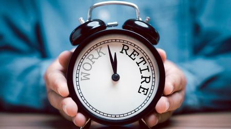 Pair of hands holding black alarm clock with clockwise countdown from work to retirement