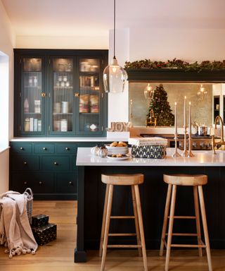 A green kitchen with a Christmas garland hung over the hob mantelpiece