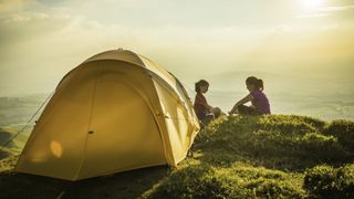 Children camping yellow tent on idyllic mountain top summer sunset