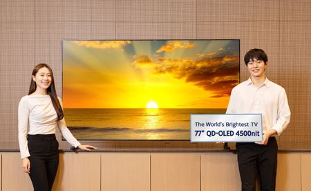 Two models in white tops and black trousers show a 77-inch Samsung 2026 QD-OLED panel TV