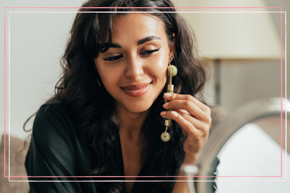 a close up of a woman with dark hair learning how to use a jade roller on her face