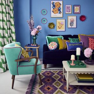 A blue-painted living room decorated with Sophie Robinson's pieces from her collection for Dunelm including colourful cushions, candle holders and a wavy tray