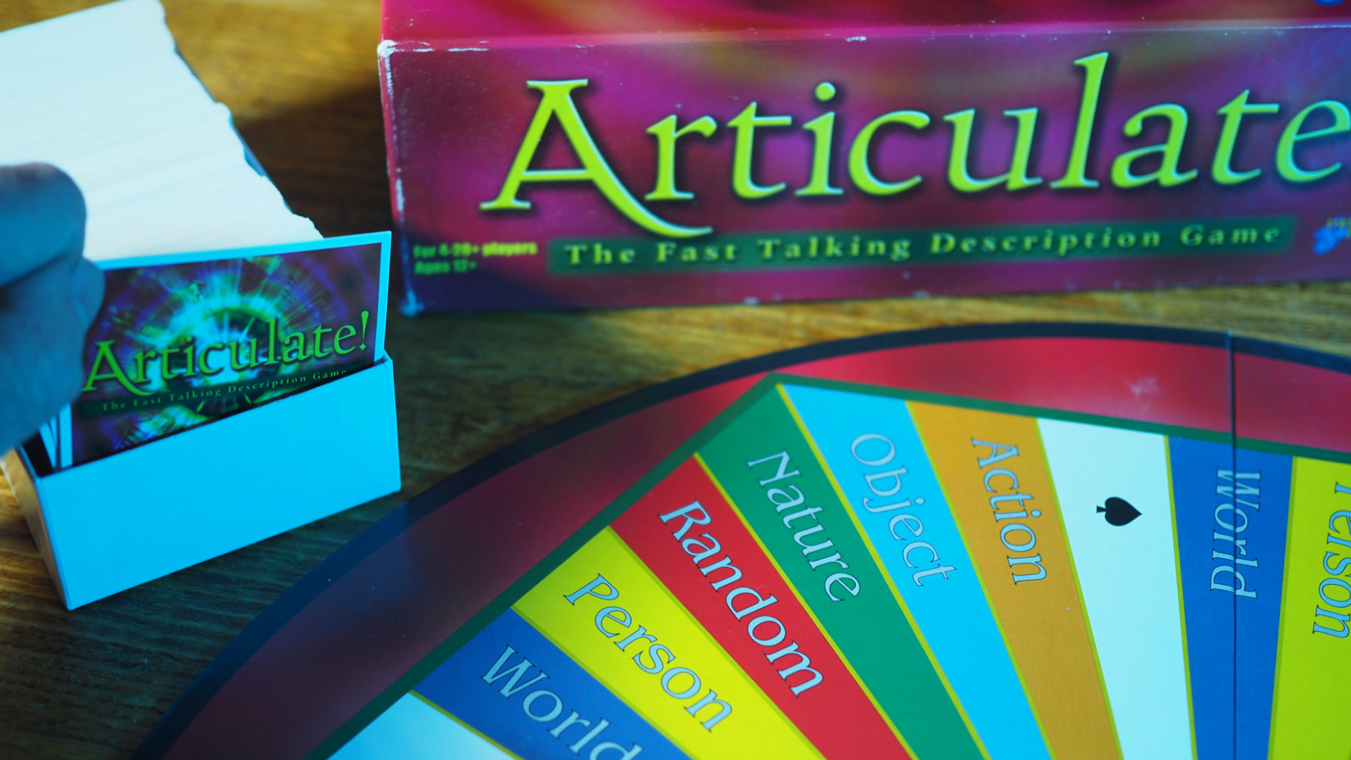 A hand lifts an articulated card of a case along with the games box and the board