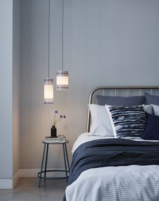 blue bedroom with iron bed, shades of blue bedding, two pendant lights hanging above side table