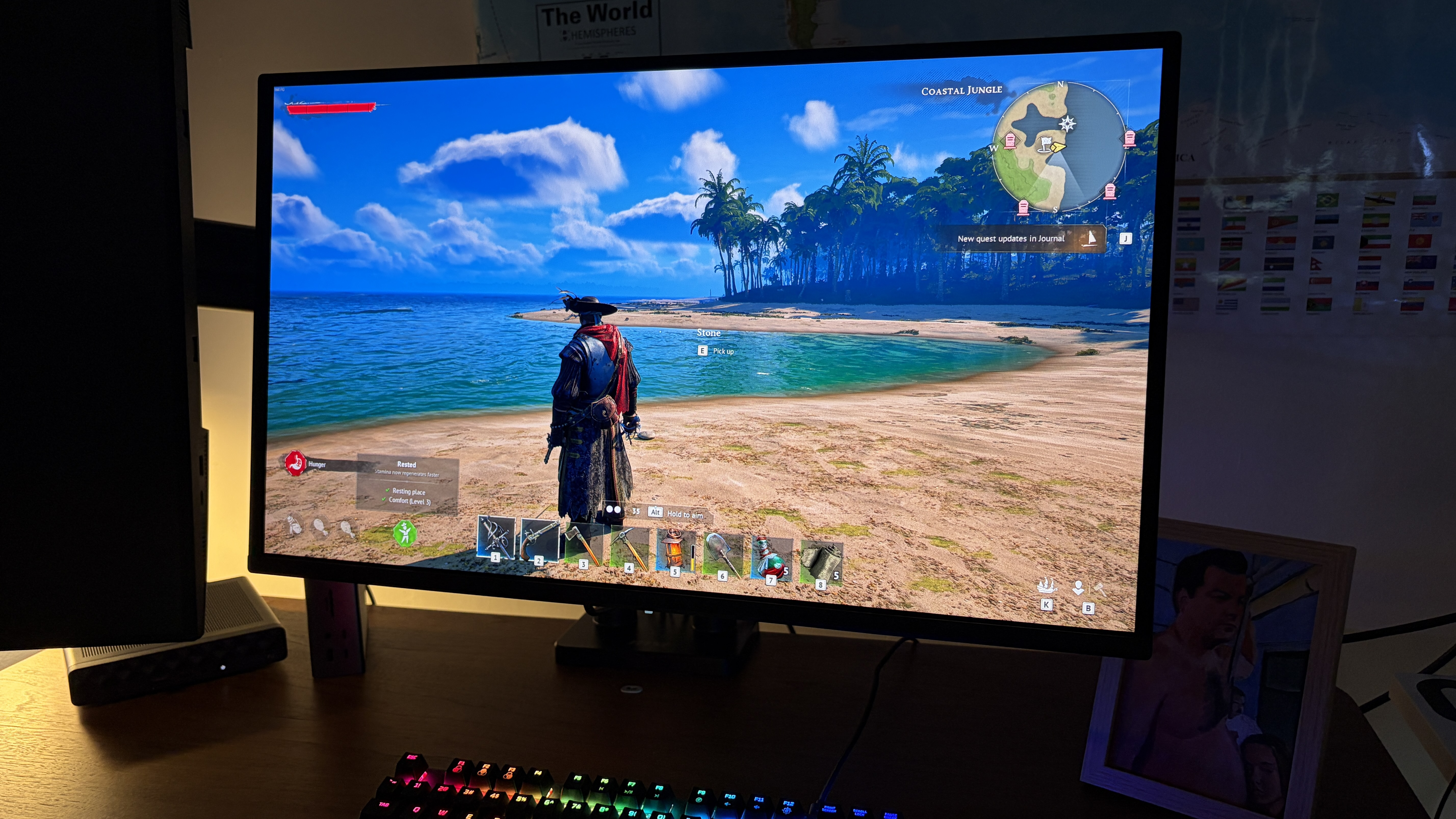 A computer screen displays a pirate-themed video game, showing a pirate on a tropical beach. A rainbow-lit keyboard is in front, creating a gaming atmosphere.