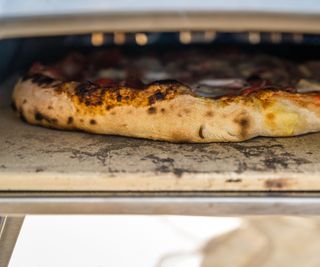 A close up of a pizza cooking on a blackened pizza stone