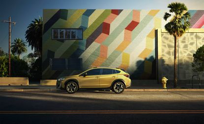 Daytime outside image of a yellow Subaru XV E-Boxer, road, yellow water hydrant, palm tree, colourful block pattern wall, clear blue sky