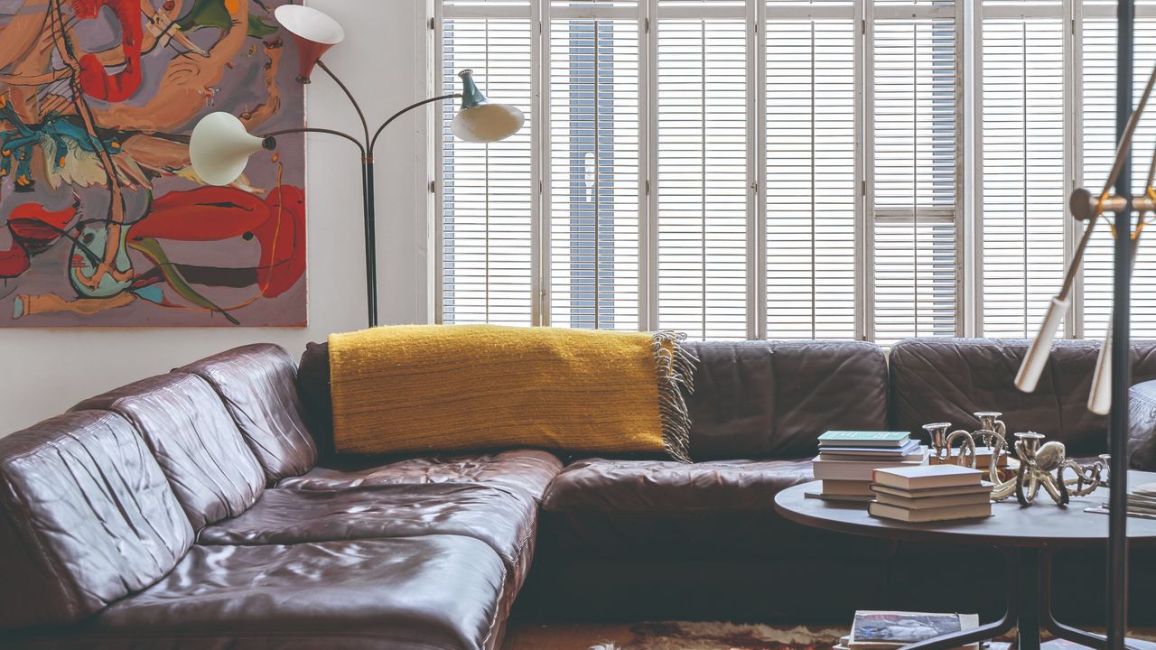 A living room with a large corner brown leather sofa and a colourful abstract painting behind it