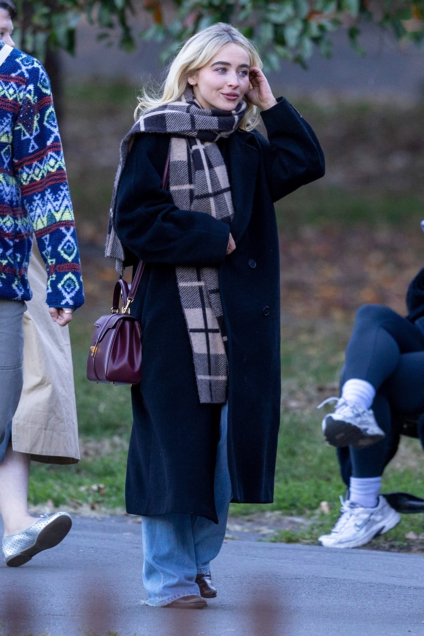 Sabrina Carpenter wearing a black Aritiza coat, plaid scarf, jeans, and a burgundy Celine bag in Central Park