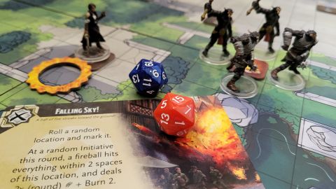 A card, dice, and miniatures sit on an illustrated board from Trials of Tempus