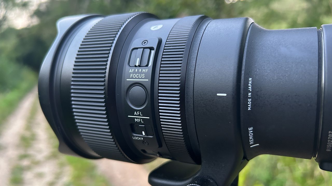 A black camera lens with two ridged adjustment rings is mounted to an out-of-frame tripod and attached to a rectangular black camera.