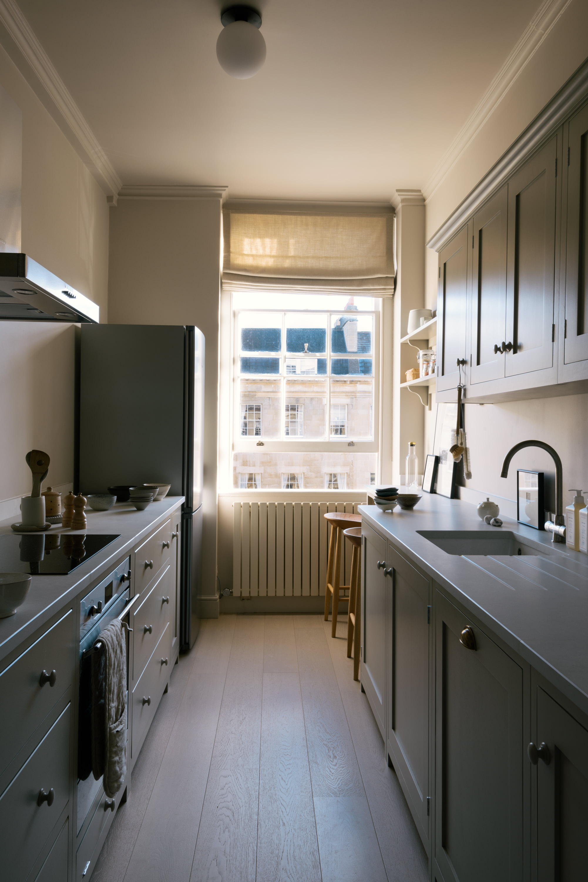A light muted galley kitchen with a large sash window at the end