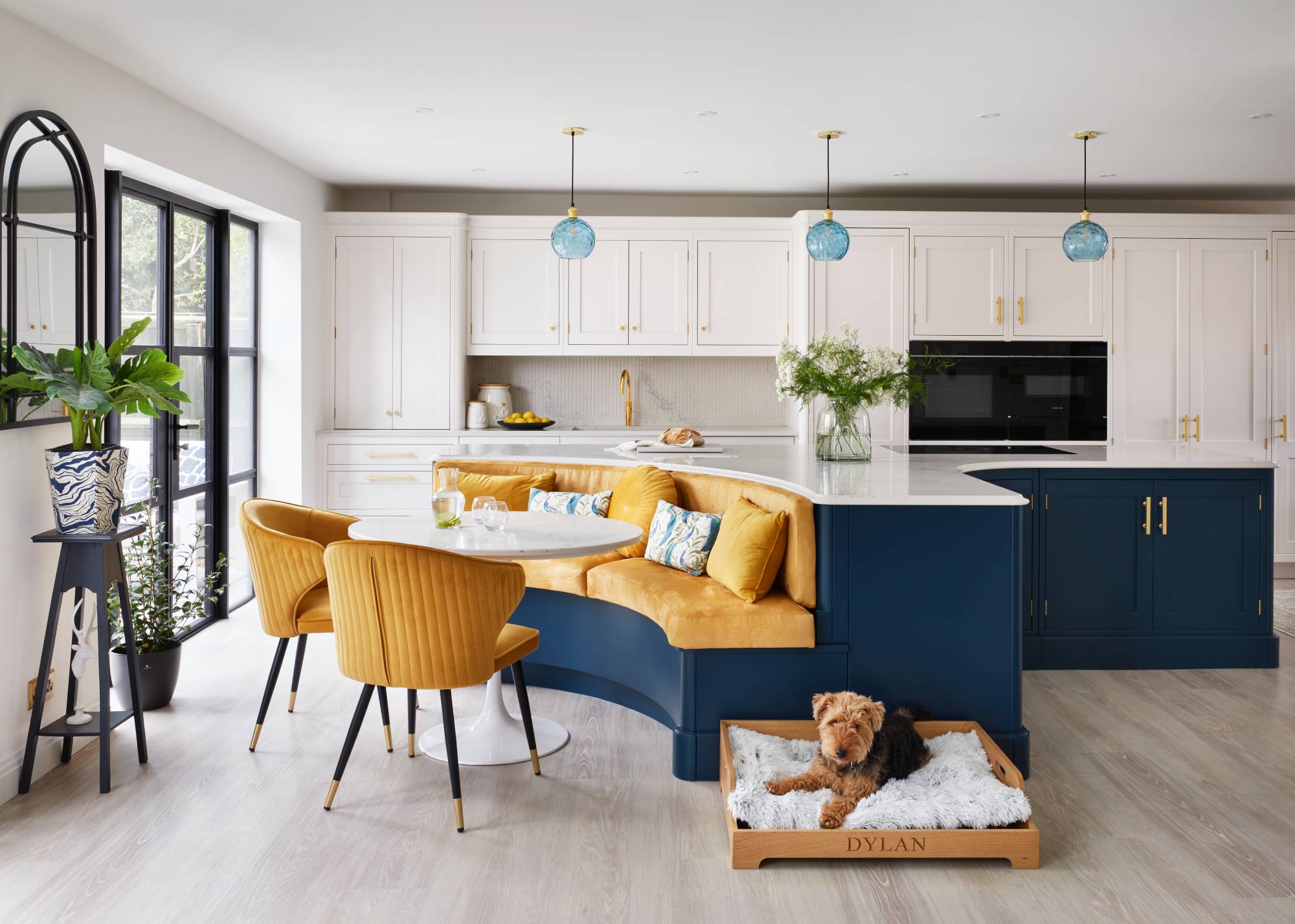 dark blue kitchen island in white kitchen with yellow banquette seating and dog bed
