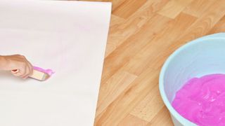Hand adding paste to wall paper with pink wallpaper paste in a bucket