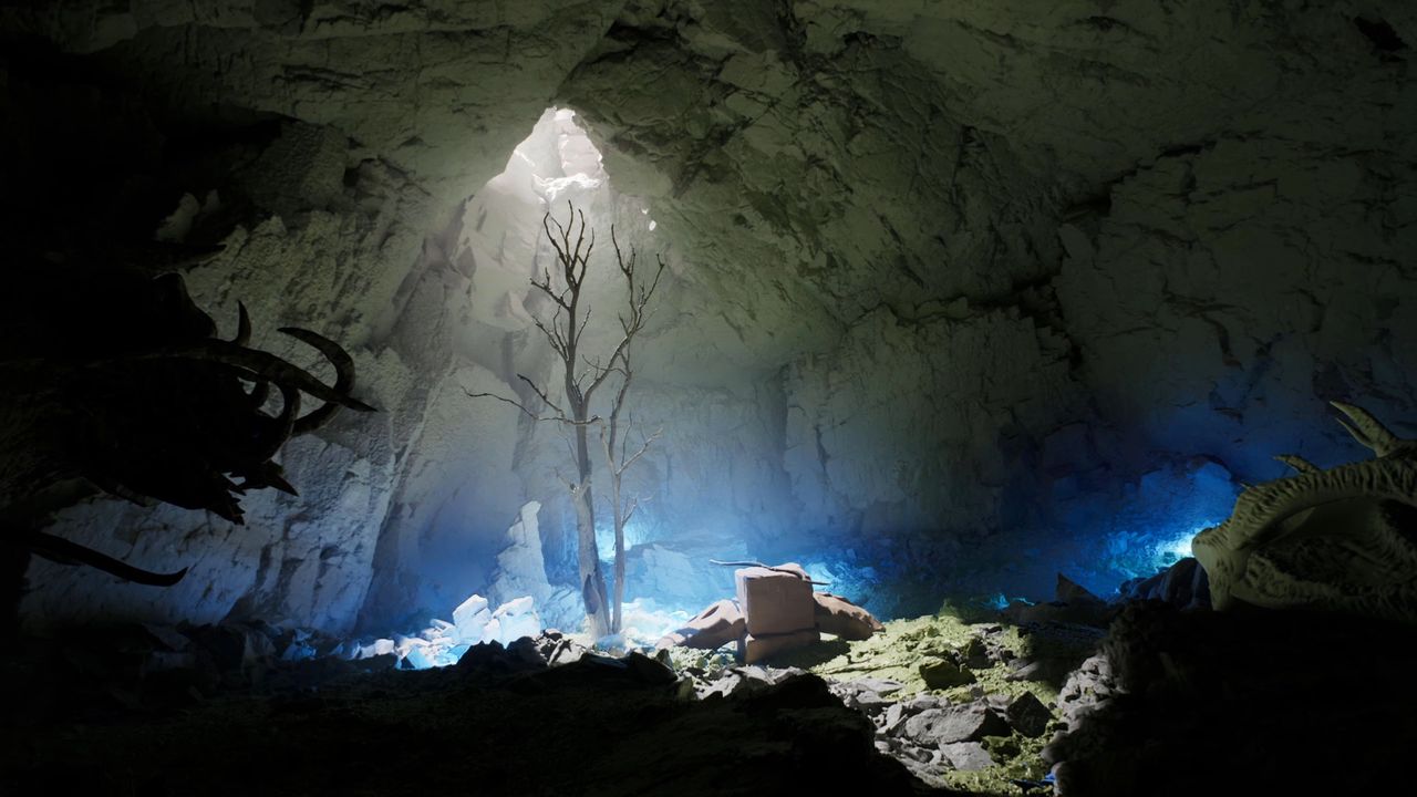 a single tree thrusts towards an opening in a cave ceiling with light shafts streaming down